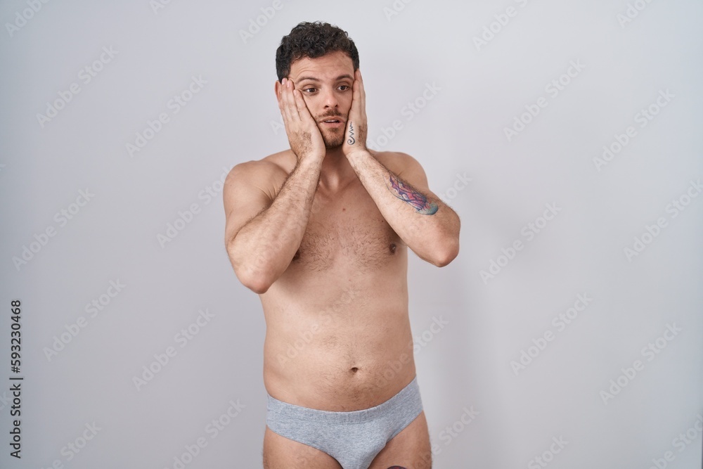 Fototapeta premium Young hispanic man standing shirtless wearing underware tired hands covering face, depression and sadness, upset and irritated for problem