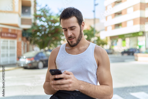 Young hispanic man smiling confident using smartphone at street