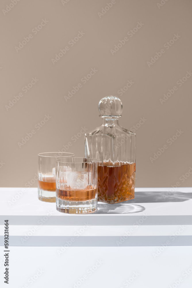Dos vasos de whisky con hielo y decantador sobre un fondo beige Dos vasos de whisky con hielo y decantador sobre un fondo beige