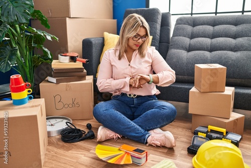 Принти на полотні Young hispanic woman moving to a new home sitting on the floor checking the time