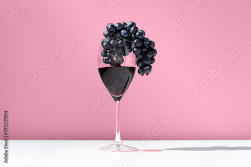 Copa de vino tinto con uvas negras sobre fondo rosa	 photo