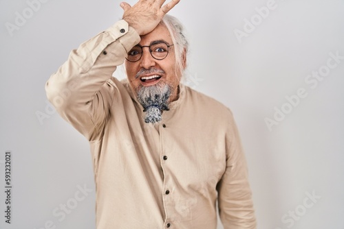 Middle age man with grey hair standing over isolated background surprised with hand on head for mistake, remember error. forgot, bad memory concept. © Krakenimages.com