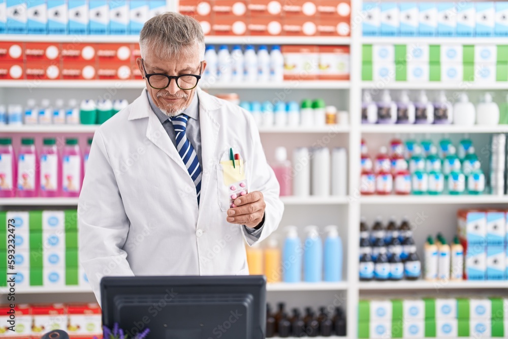 Middle age grey-haired man pharmacist holding pills tablet using computer at laboratory Middle age grey-haired man pharmacist holding pills tablet using computer at laboratory