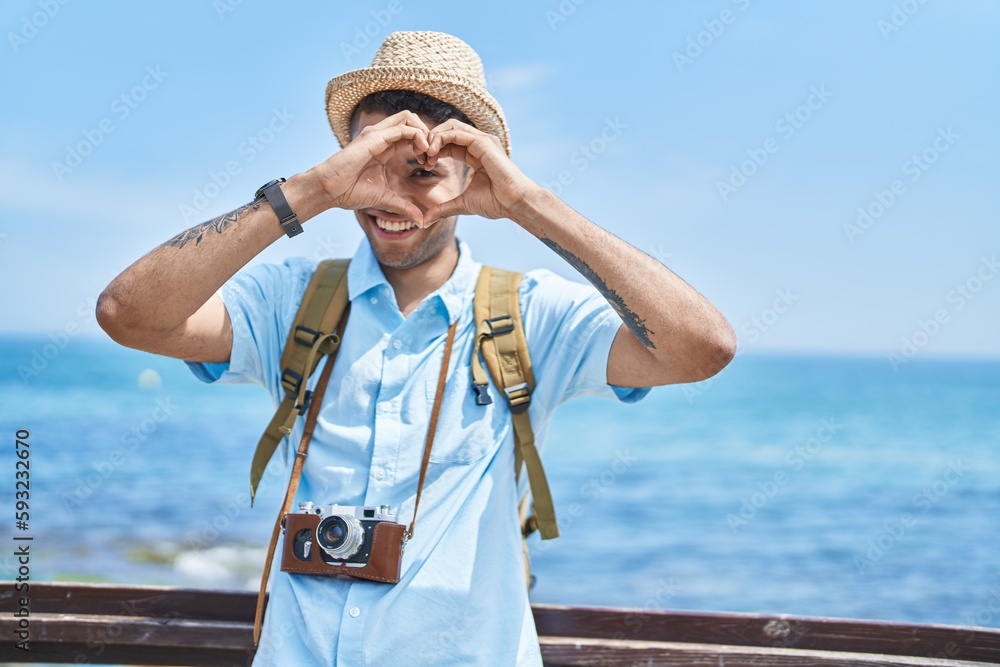 African american man tourist smiling confident doing heart gesture at seaside