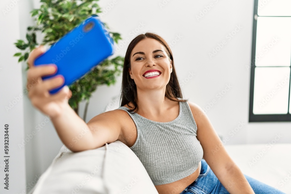 Young beautiful hispanic woman make selfie by smartphone sitting on sofa at home Young beautiful hispanic woman make selfie by smartphone sitting on sofa at home
