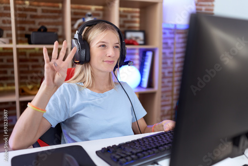 Young caucasian woman playing video games wearing headphones showing and pointing up with fingers number four while smiling confident and happy.