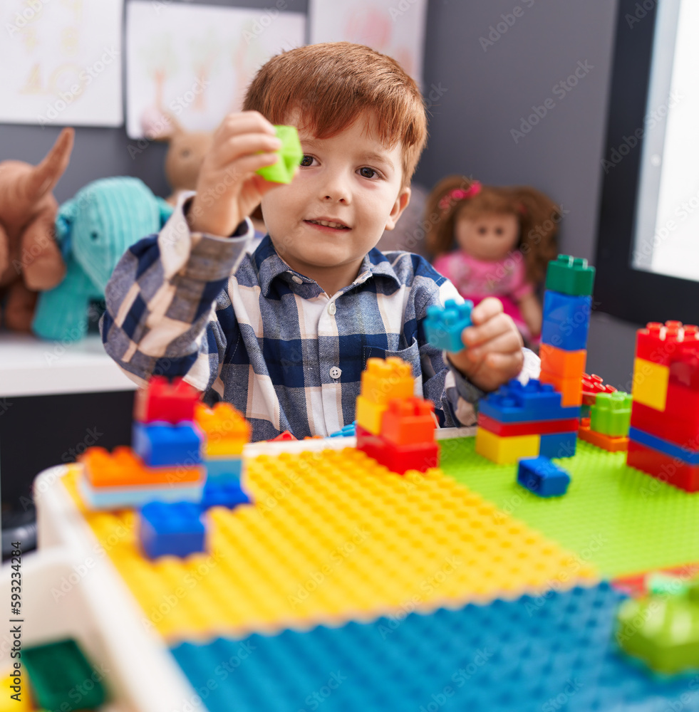 Fototapeta premium Adorable toddler playing with construction blocks sitting on table at kindergarten