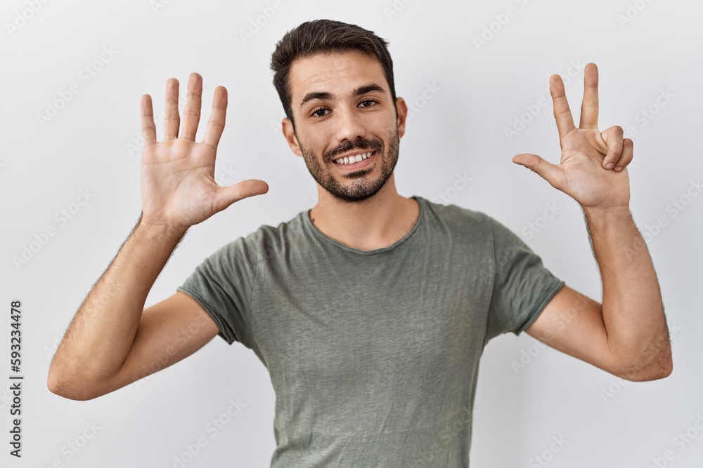 Young hispanic man with beard wearing casual t shirt over white background showing and pointing up with fingers number eight while smiling confident and happy. Young hispanic man with beard wearing casual t shirt over white background showing and pointing up with fingers number eight while smiling confident and happy.