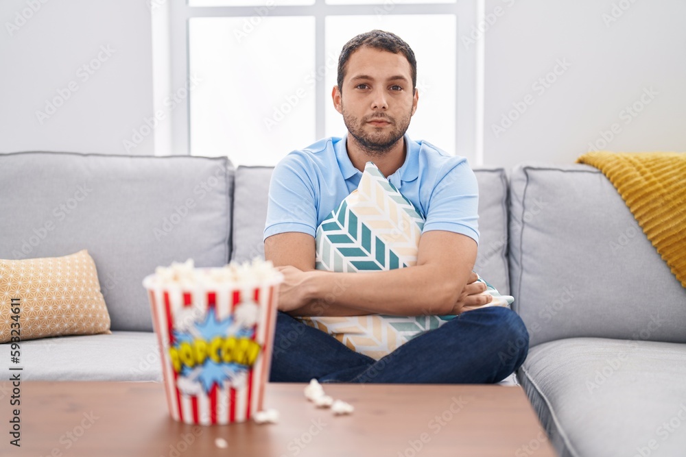 Hispanic man watching tv at home sitting on the sofa relaxed with serious expression on face. simple and natural looking at the camera. Hispanic man watching tv at home sitting on the sofa relaxed with serious expression on face. simple and natural looking at the camera.