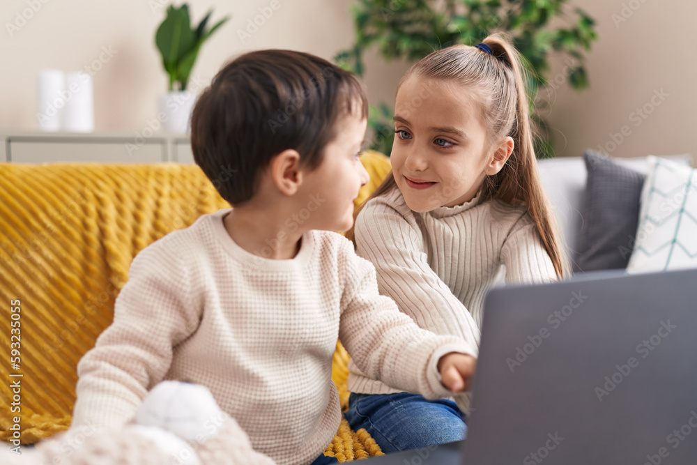 Adorable boy and girl using laptop sitting on sofa at home Adorable boy and girl using laptop sitting on sofa at home