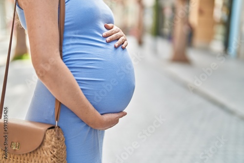 Young pregnant woman touching belly at street