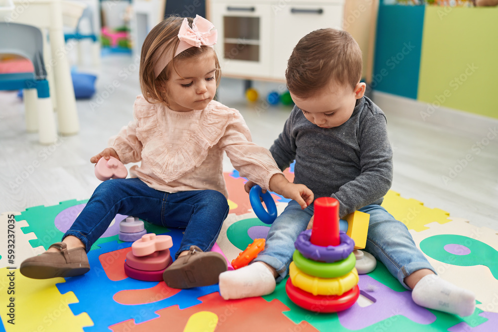 Adorable boy and girl playing with hoops game sitting on floor at kindergarten Adorable boy and girl playing with hoops game sitting on floor at kindergarten