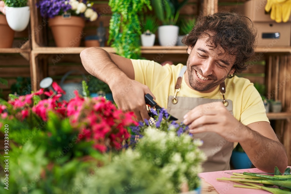 Young hispanic man florist smiling confident cutting plant at flower shop
