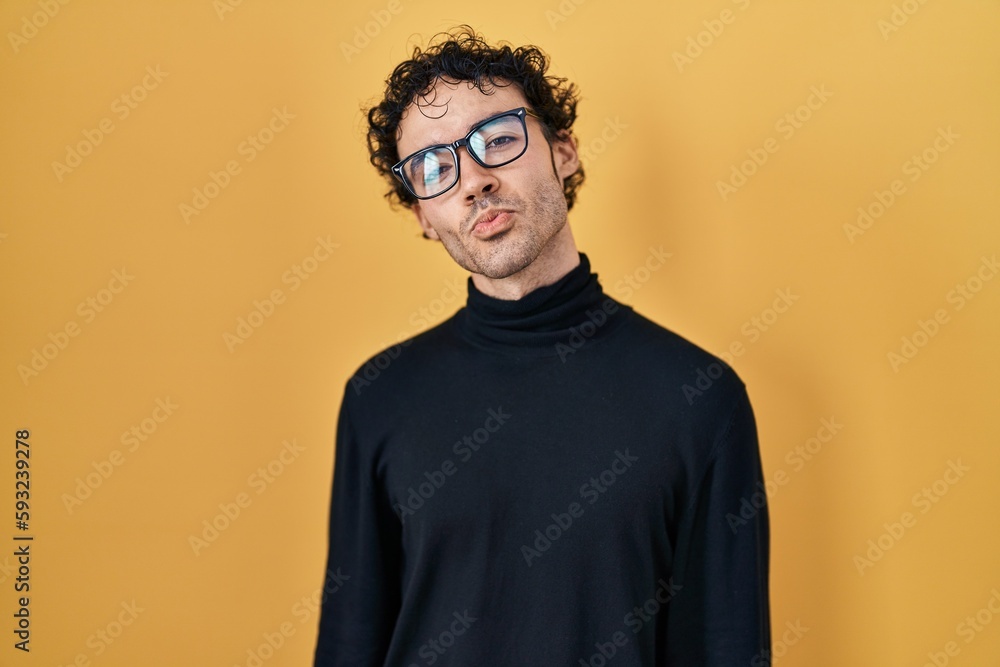 Fototapeta premium Hispanic man standing over yellow background looking at the camera blowing a kiss on air being lovely and sexy. love expression.