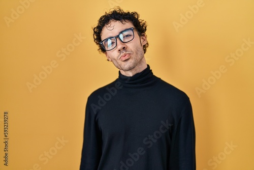 Hispanic man standing over yellow background looking at the camera blowing a kiss on air being lovely and sexy. love expression.