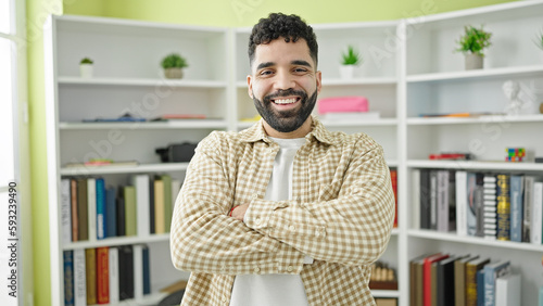 Young hispanic man student smiling confident standing with arms crossed gesture at library university