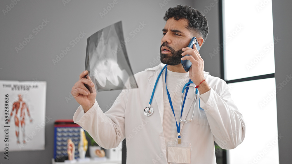 Young hispanic man doctor looking xray talking on smartphone at clinic Young hispanic man doctor looking xray talking on smartphone at clinic
