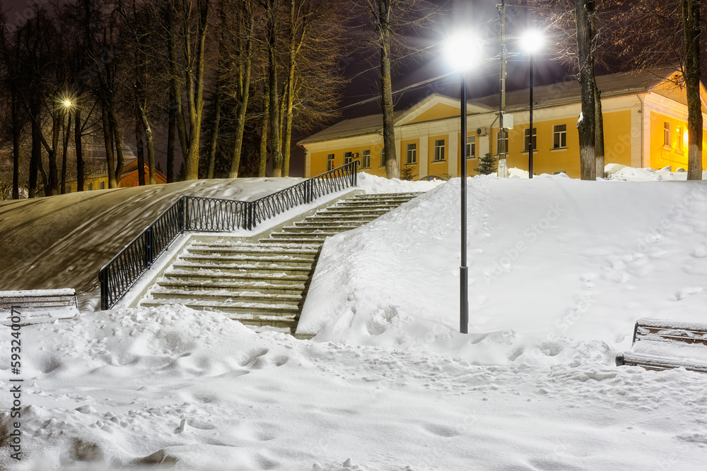 Winter city landscape in the light of street lighting. View from the snow-covered stairs from embankment to the administration of Torzhok.