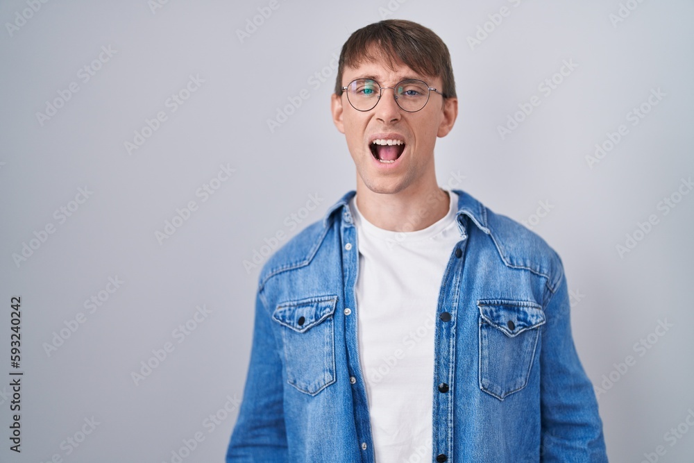 Caucasian blond man standing wearing glasses angry and mad screaming frustrated and furious, shouting with anger. rage and aggressive concept. Caucasian blond man standing wearing glasses angry and mad screaming frustrated and furious, shouting with anger. rage and aggressive concept.