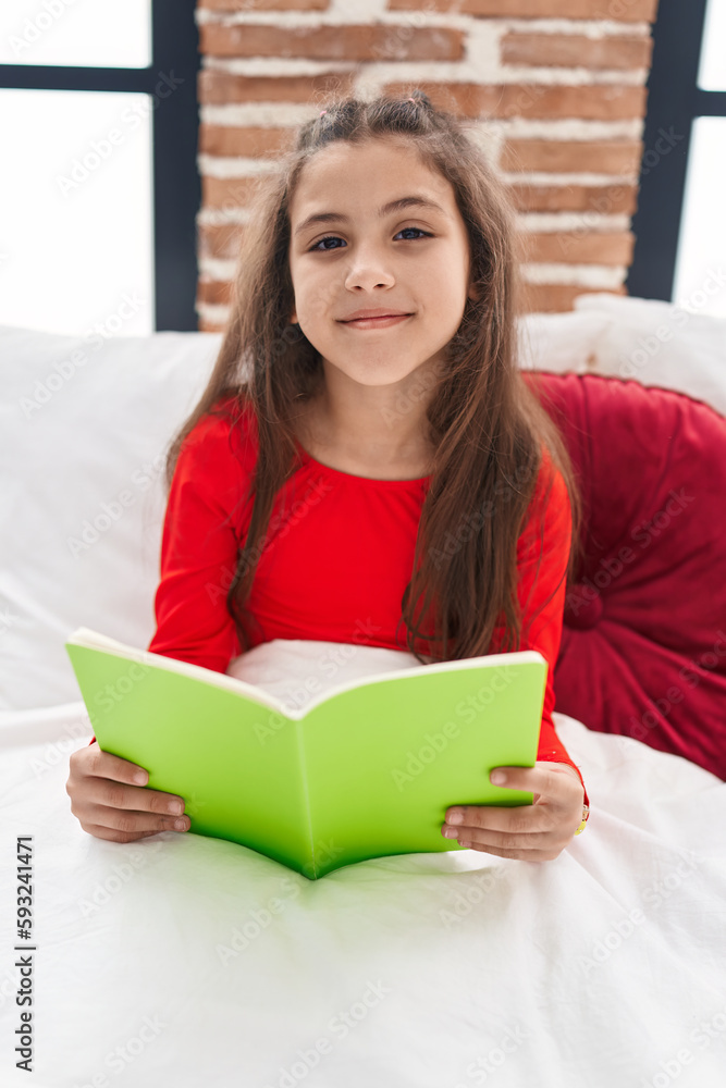 Adorable hispanic girl reading book sitting on bed at bedroom Adorable hispanic girl reading book sitting on bed at bedroom