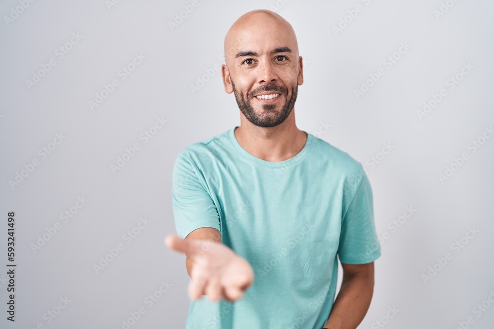 Middle age bald man standing over white background smiling cheerful offering palm hand giving assistance and acceptance. Middle age bald man standing over white background smiling cheerful offering palm hand giving assistance and acceptance.