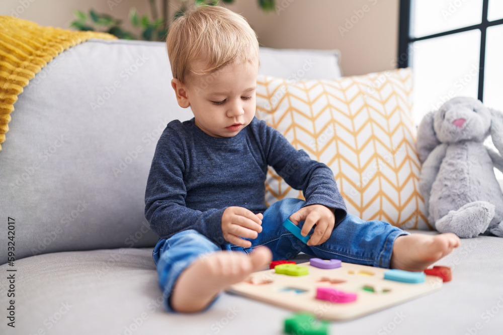 Adorable blond toddler playing with maths game sitting on sofa at home Adorable blond toddler playing with maths game sitting on sofa at home
