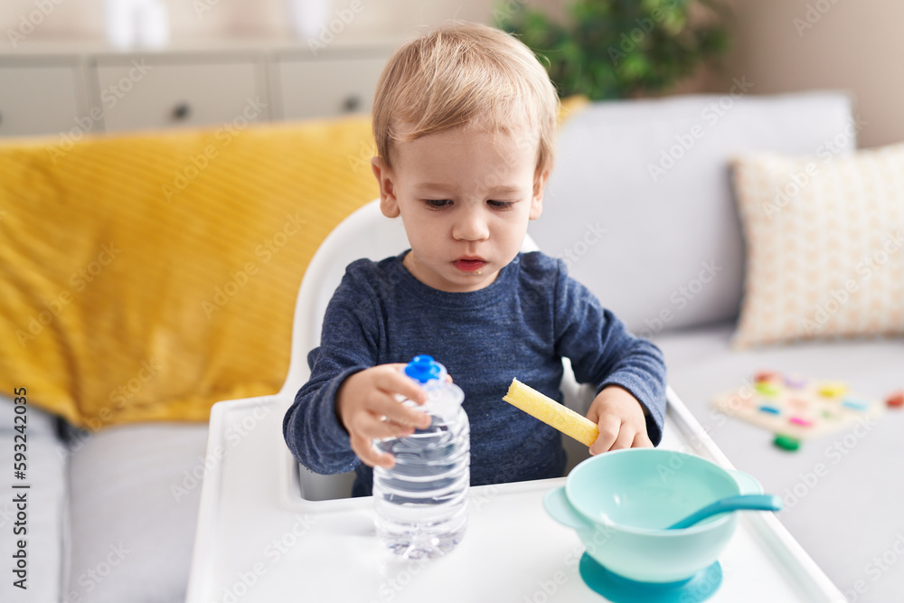 Adorable blond toddler sitting on highchair eating snack at home Adorable blond toddler sitting on highchair eating snack at home