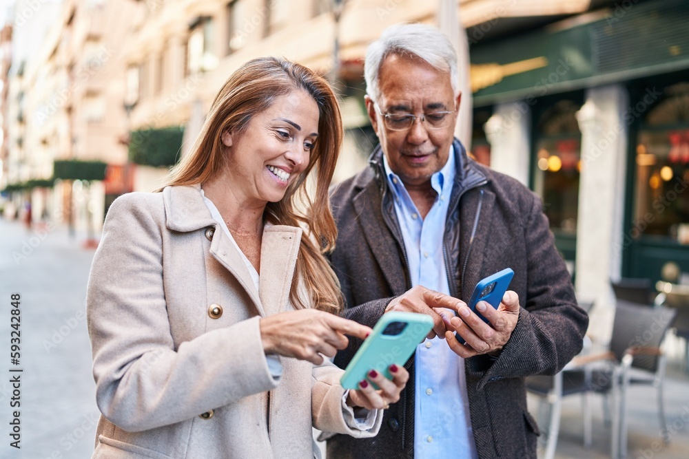 Middle age man and woman couple smiling confident using smartphone at street