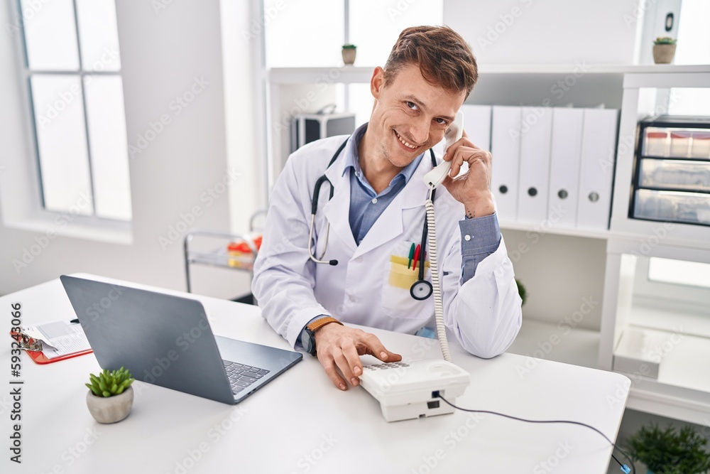 Young man doctor using laptop talking on telephone at clinic Young man doctor using laptop talking on telephone at clinic