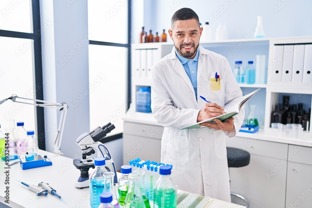 Young latin man scientist smiling confident writing on notebook at laboratory Young latin man scientist smiling confident writing on notebook at laboratory