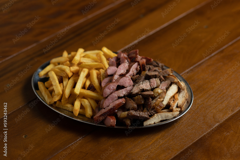 Fototapeta premium Porção de fritas, filé e linguiça em fundo rústico de madeira