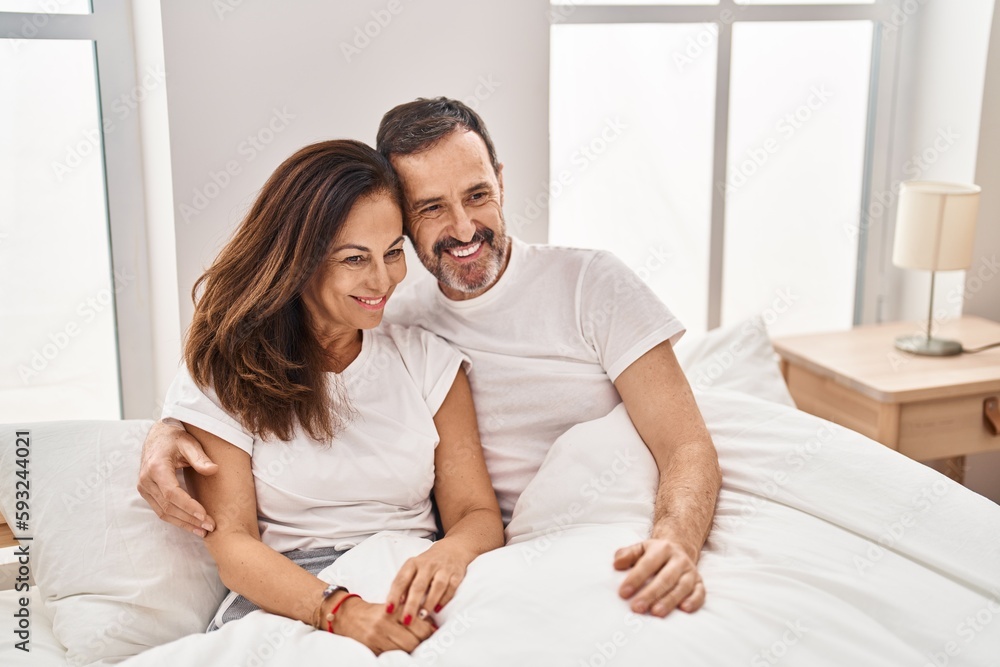 Middle age man and woman couple hugging each other sitting on bed at bedroom Middle age man and woman couple hugging each other sitting on bed at bedroom