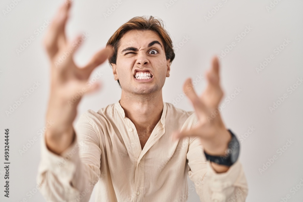 Young man standing over isolated background shouting frustrated with rage, hands trying to strangle, yelling mad Young man standing over isolated background shouting frustrated with rage, hands trying to strangle, yelling mad