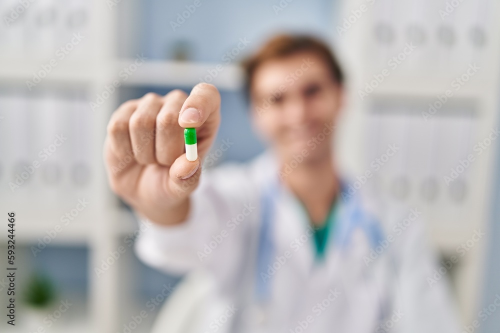 Young caucasian man doctor holding pill at clinic