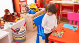 Adorable caucasian boy playing with maths puzzle game sitting on table at kindergarten