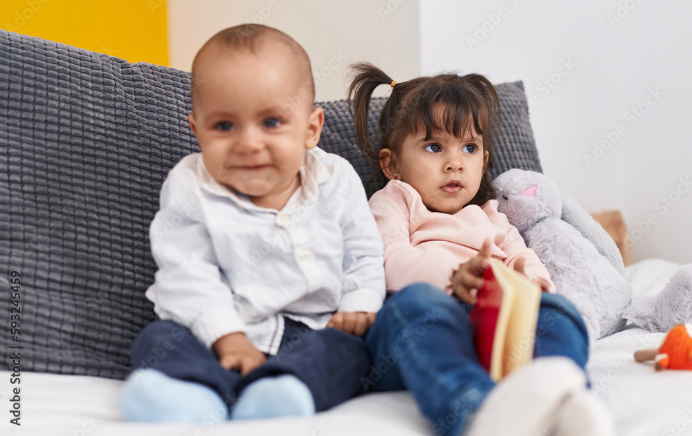 Adorable boy and girl reading book sitting on bed at home Adorable boy and girl reading book sitting on bed at home