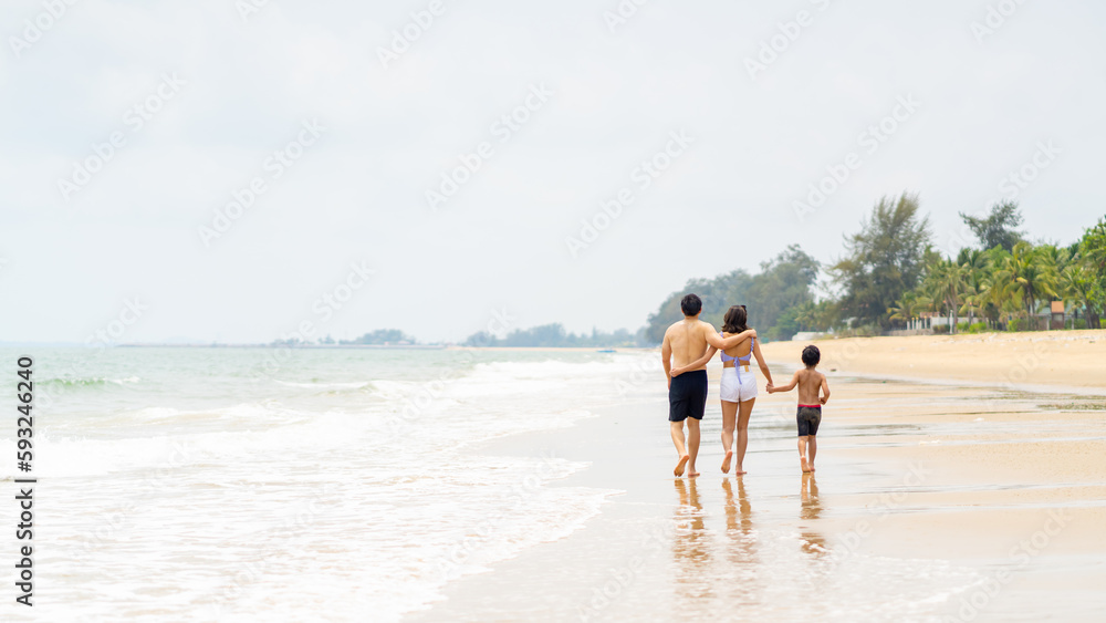 Happy Asian family travel ocean on summer holiday vacation. Parents and little son in swimwear have fun outdoor activity lifestyle walking and playing sea water together at tropical beach in sunny day Happy Asian family travel ocean on summer holiday vacation. Parents and little son in swimwear have fun outdoor activity lifestyle walking and playing sea water together at tropical beach in sunny day