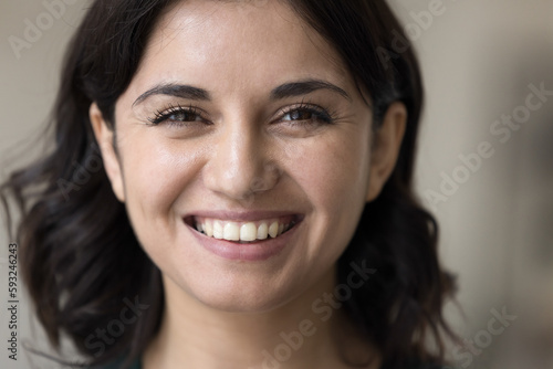 Close-up front view young 25s beautiful brunette brown-eyed Armenian woman, smile, look at camera, feels happy, having attractive appearance, positive emotions, millennial generation female portrait