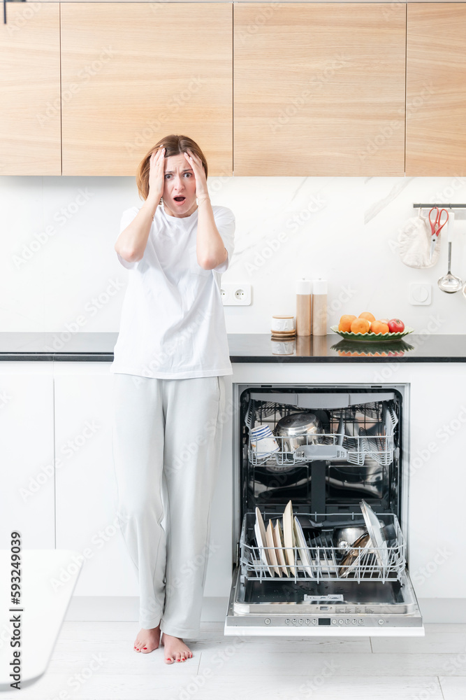 Tired and bored woman putting dirty plates in dishwasher machine in the kitchen. Household and exhausting cleaning day concept Tired and bored woman putting dirty plates in dishwasher machine in the kitchen. Household and exhausting cleaning day concept