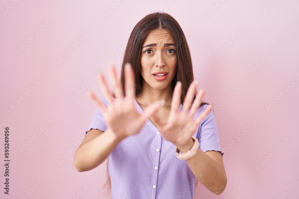 Young hispanic woman with long hair standing over pink background afraid and terrified with fear expression stop gesture with hands, shouting in shock. panic concept. Young hispanic woman with long hair standing over pink background afraid and terrified with fear expression stop gesture with hands, shouting in shock. panic concept.