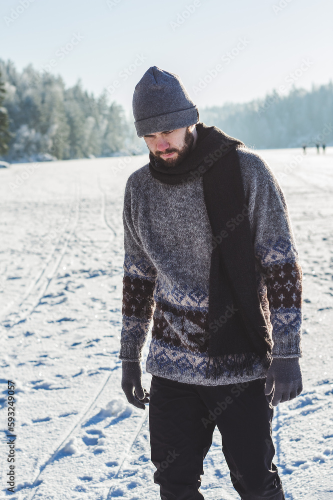 man walking in snowy frozen lake on winter day with knitted sweather looking down