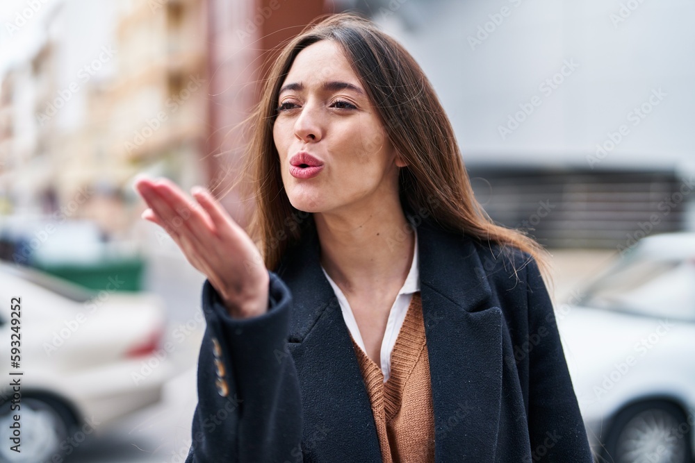 Young beautiful hispanic woman smiling confident doing kiss gesture with hand at street