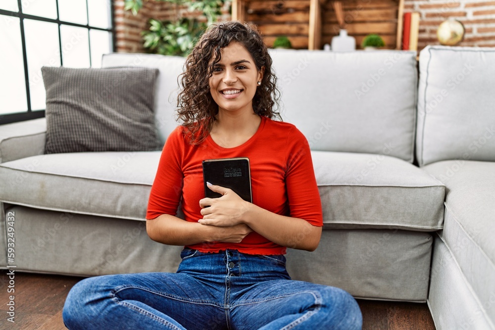 Obraz premium Young latin woman smiling confident hugging bible at home