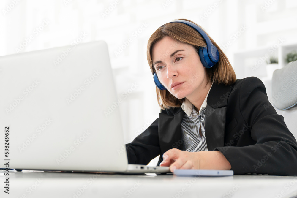 Portrait of successful and attractive business woman working on laptop in her office. Positive female employee in black suit smiling and sitting at the desk in her modern workplace Portrait of successful and attractive business woman working on laptop in her office. Positive female employee in black suit smiling and sitting at the desk in her modern workplace