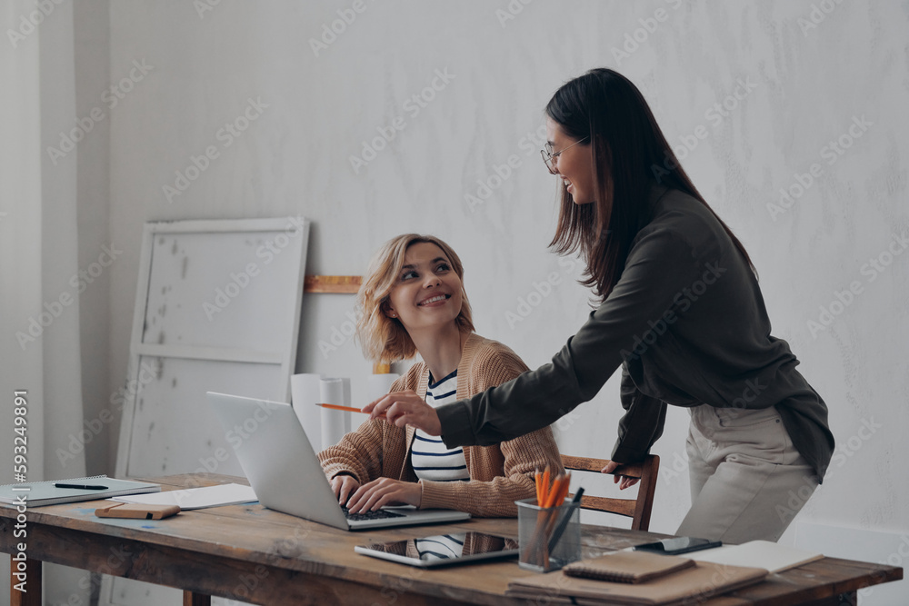 Two happy young women discussing business while working together at the creative office Two happy young women discussing business while working together at the creative office