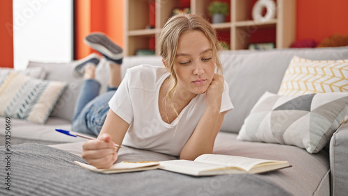 Young blonde woman reading book writing on notebook at home