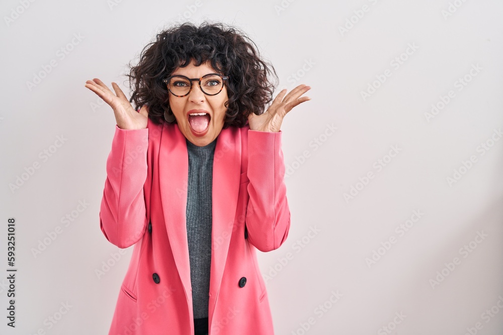 Hispanic woman with curly hair standing over isolated background celebrating crazy and amazed for success with arms raised and open eyes screaming excited. winner concept Hispanic woman with curly hair standing over isolated background celebrating crazy and amazed for success with arms raised and open eyes screaming excited. winner concept