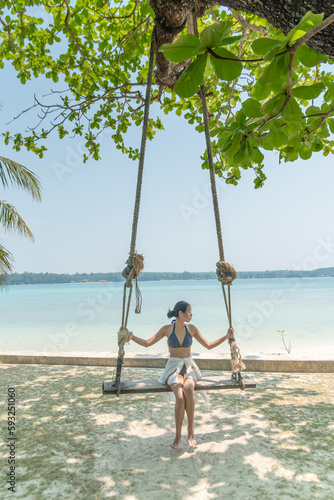 Female traveler play wooden swing under the giant tree on the beach  relax on vacation