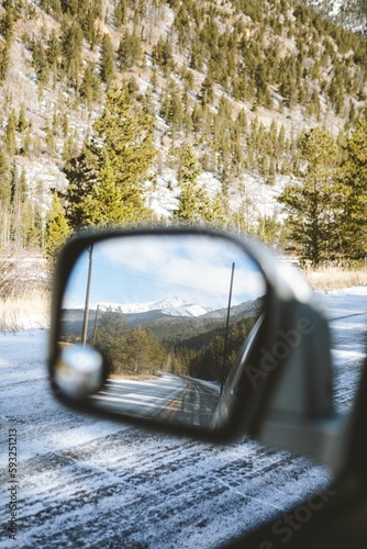 Road covered in snow with a stunning landscape in the side mirror of a truck