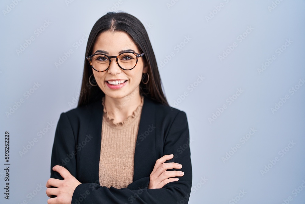 Young brunette woman standing over blue background happy face smiling with crossed arms looking at the camera. positive person. Young brunette woman standing over blue background happy face smiling with crossed arms looking at the camera. positive person.